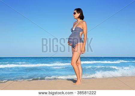 Bella donna incinta in piedi sulla spiaggia blu in vacanza estiva