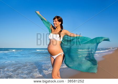 Bella donna incinta camminando sulla spiaggia blu in estate con il fazzoletto di vento di salto
