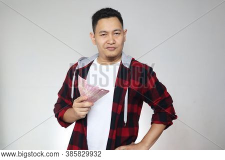 Portrait Of Happy Young Indonesian Man Holding Rupiah Money, Smiling Laughing Winning Gesture, Over 