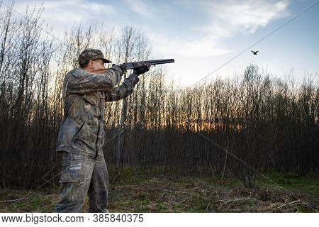 A Hunter Stands At Dusk In A Forest Clearing And Takes Aim A Low-flying Male Woodcock, Which Makes A