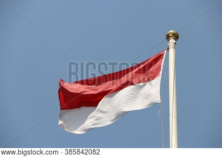 National Flag Of Indonesia On Bright Blue Sky Background. Blown Away By Wind. Indonesia Is One Of Th