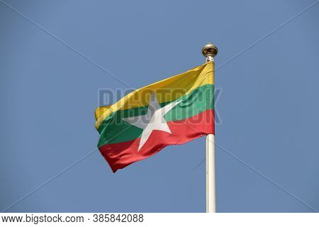 National Flag Of Myanmar On Bright Blue Sky Background. Blown Away By Wind. Myanmar Is One Of The Te