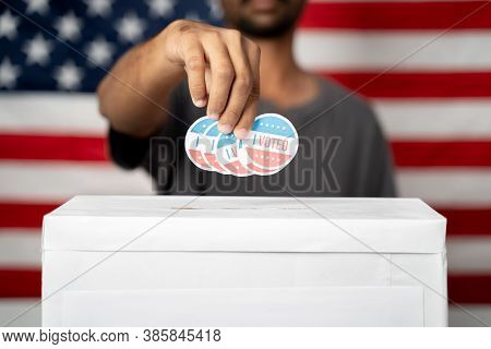 Close Up Of Hands Dropping Multiple I Voted Sticker Inside Ballot Box With Us Flag As Background, Co