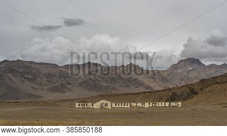 Abandoned Farm And Orange Colored Mountains With Snow At The Pamir Highway In Tajikistan Near Alichu