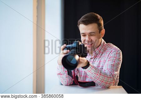 A Male Photographer In A Checkered Shirt Sits At A Table And Holds A Camera In His Hands. Creative P