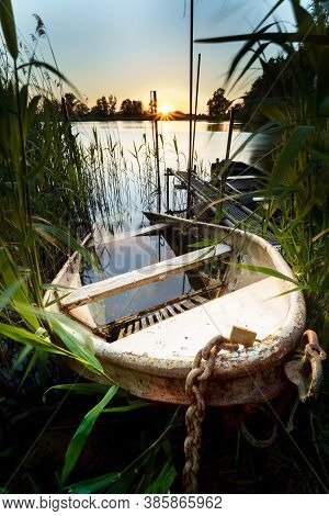 Old Iron Rowing Boat Sunk Half Way On The Waterfront Of A Pond At Sunset