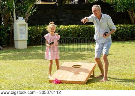 Happy Family Playing Cornhole Game Outdoor On Sunny Summer Day. Parents And Children Playing Bean Ba