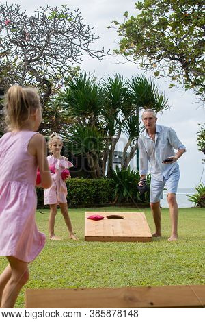 Happy Family Playing Cornhole Game By The Sea On Sunny Summer Day. Parents And Children Playing Bean