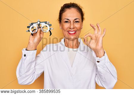 Middle age senior oculist woman holding optometrical glasses for vision correction doing ok sign with fingers, excellent symbol