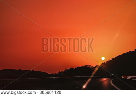 Vibrant Orange Red Deep Colors Sunset Sky Over Highway With One Car Driving And Sun Over Mountains S