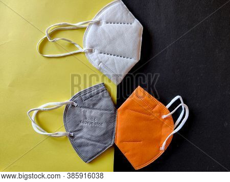 Three Kn-95 Face Masks In White,grey And Orange Color. Isolated On Black And Yellow Background. Prot