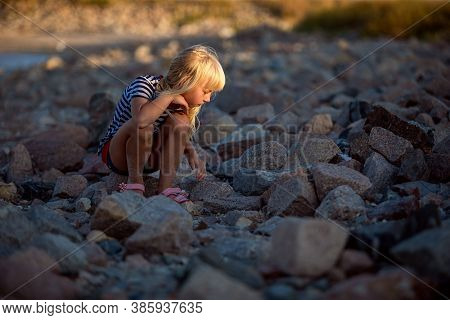 Little Girl Plays On Stones, She Is Looking For A Lost Toy.