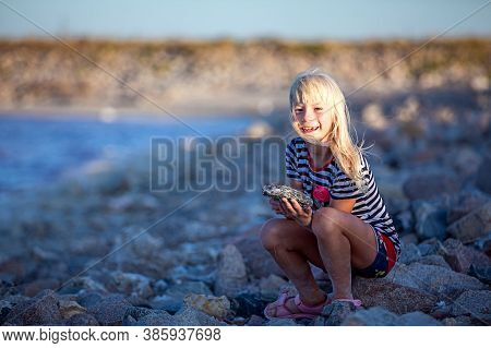 Little Girl Plays A Stone By The River. She Has Fun.