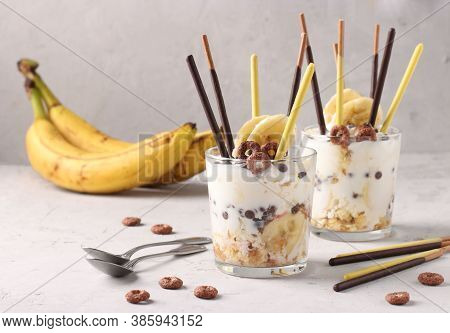 Two Glasses Of Granola With Chocolate And Banana, Decorated With Sticks Pocky On Gray Background, Ho