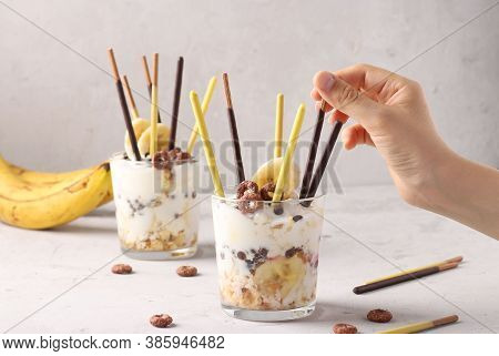 Two Glasses Of Granola With Chocolate And Banana, Decorated With Sticks Pocky On Gray Background