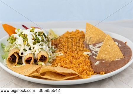 Taquitos Covered In Cheese With Rice And Beans Served On A Hot Plate For Some Delicious Mexican Food