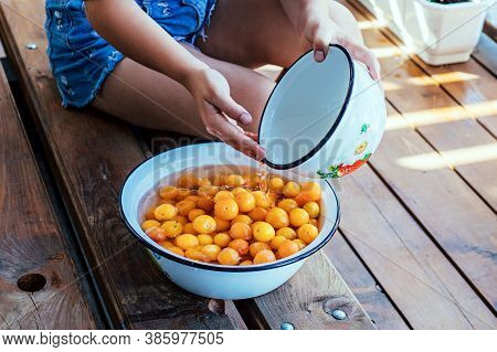 Girl Washes Yellow Fruits With Her Hands In A Bowl Of Water. Healthy Eating, Traditional Lifestyle.