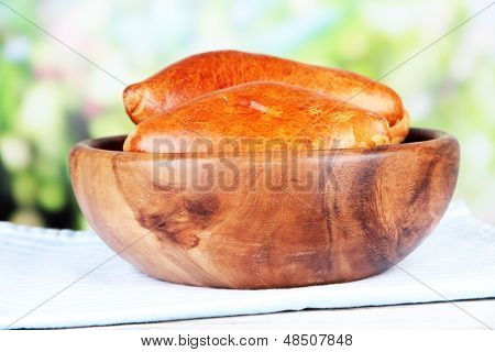 Empanadillas al horno frescos, en un recipiente de madera, en la mesa de madera, sobre fondo brillante