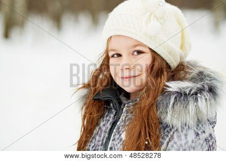 Closeup helft-gedraaide portret van meisje in grijze jas met bont kraag en gebreide muts in snowy 