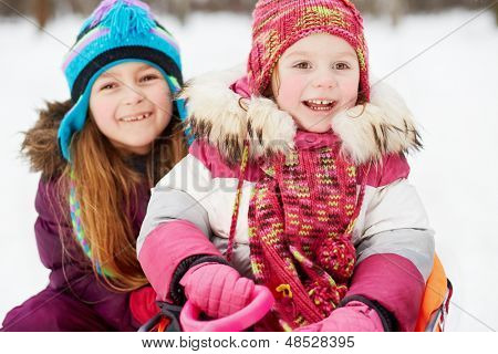 Lachen jongere meisje zit in de slee, oudere zit gehurkte achter haar, winter park