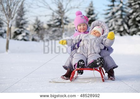 Duas crianças vestidas com roupas quentes, perto de floresta sente-se no trenó vermelho no inverno.