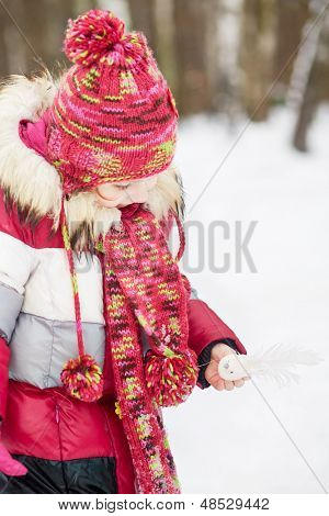Klein meisje staat in winter park met kleine witte kunstmatige vogel in haar hand