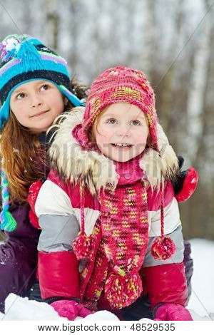 Oudere meisje omarmt haar jongere zus achter zittend op sneeuw