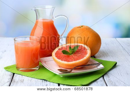 Half of grapefruit, glass jug with fresh juice and spoon on plate on light background
