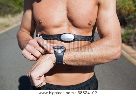 Athletic man on open road with monitor around chest on a sunny day