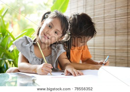 Cute ?little pan asian girl holding a coloring pencil sitting next to an older brother engrossed in coloring activity in home environment