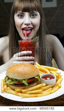 Girl drinking juice and eating burger with fries in cafeteria
