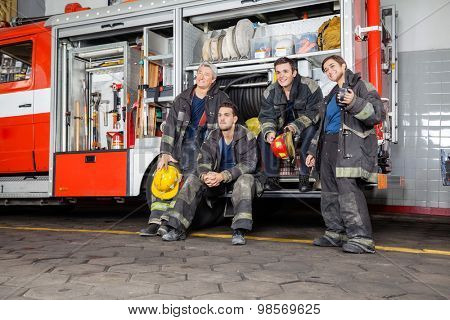 Team of thoughtful firefighters looking away by firetruck at station