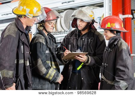 Team of firefighters discussing over clipboard while standing at fire station