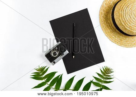 Straw hat with green leaves and old camera on white background, Summer background. Top view. Copy space. Still life. Flat lay