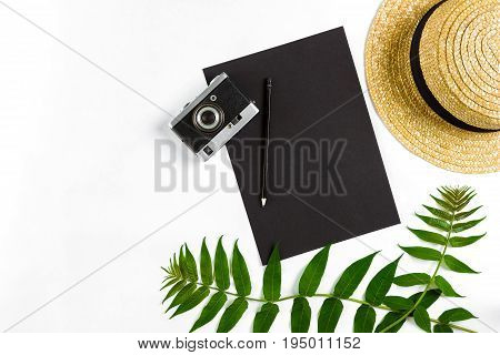Straw hat with green leaves and old camera on white background, Summer background. Top view. Copy space. Still life. Flat lay
