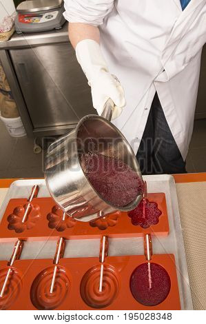 Sweets artisanal production of fruits loly pop at the factory. Close up of the saucepan pan with liquid hot red sugar dispensing to the orange mold. Artisanal production in France
