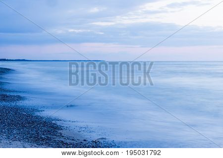 Moody empty sea and beach at dusk pebbles on beach pastel pink and blue sky tranquility and peace scene