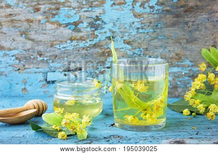 linden tea in glass on a blue background with a linden flowers and linden honey teapot. Fresh linden