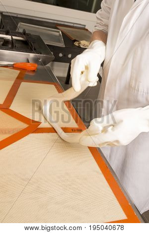 Sweets artisanal production of fruits loly pop at the factory. Close up of the hands of the employee stretching the sugar to make butterscotch fruits candies. Artisanal production in France