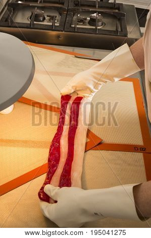 Sweets artisanal production of fruits loly pop at the factory. Close up of the hands of the employee stretching the sugar to make butterscotch fruits candies. Artisanal production in France