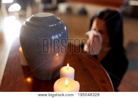 cremation, people and mourning concept - woman with wipe and cinerary urn crying at funeral in church