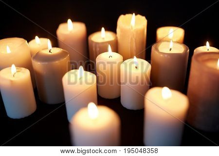 mourning and commemoration concept - candles burning in darkness over black background