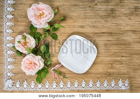 flat lay of pink roses with empty white sauser on a wooden table with lace frame and copy space for your text