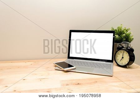 Laptop computer with white blank screen mobile smart phone and black vintage retro alarm clock times at 7 o'clock morning on wooden table workspace selective focus copy space vintage color tone