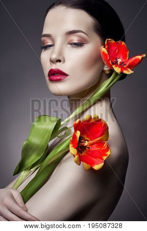 Nude Naked girl with tulips flowers in hand and perfect skin sexy naked brunette woman to gray background. Skin care of face and hands in the summer. Bright natural makeup