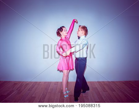 The young boy and girl posing at dance studio on blue in tango posture. The ballroom dancing concept