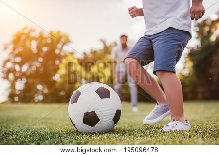 Cropped image of handsome dad with his little cute sun are having fun and playing football on green grassy lawn