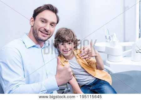 Portrait Of Smiling Dentist And Little Boy Showing Thumbs Up In Dental Clinic