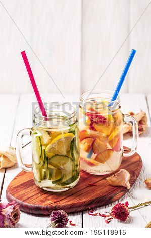 Two mugs of infused detox diet refreshing waters - first with cucumber and lemon, second with lemon and peach on white wooden table