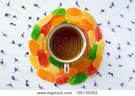 Cup of tea with candied fruits and small blue flowers on a white background